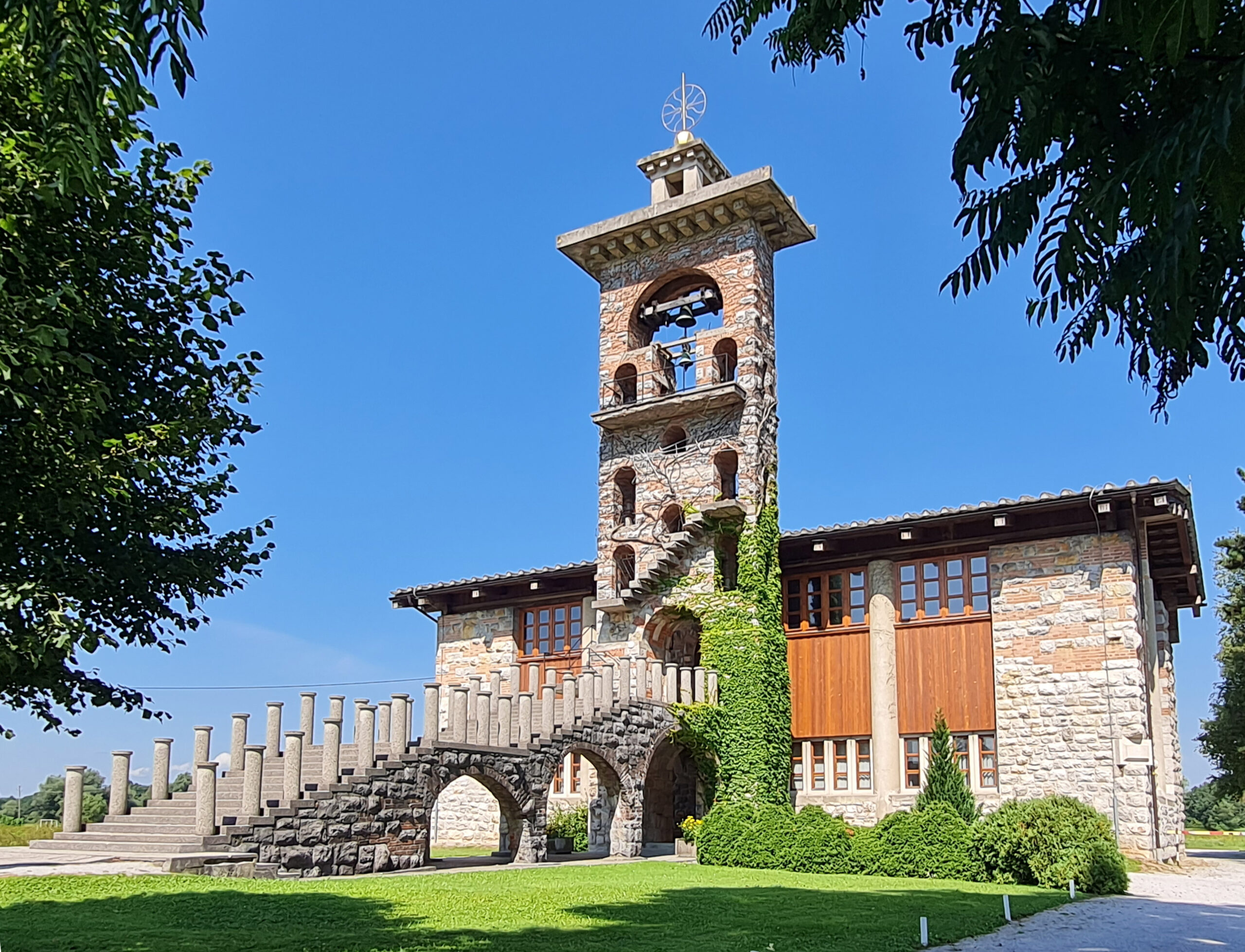 Bližnji pogled, ki poudarja kamnito in leseno konstrukcijo, z bršljanom, ki se vzpenja po zvoniku.
