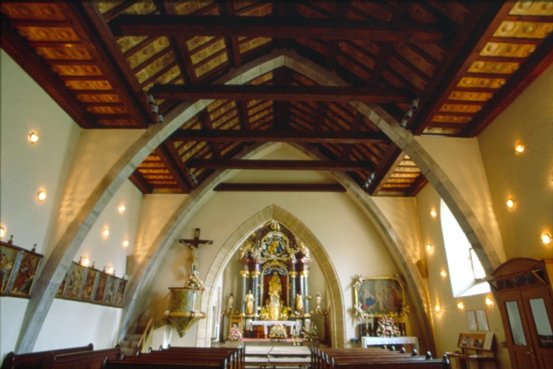 Elegantna notranjščina Cerkve Marijinega vnebovzetja pri Gradu na Goričkem, ki poudarja Plečnikove oboke in keramične podrobnosti.